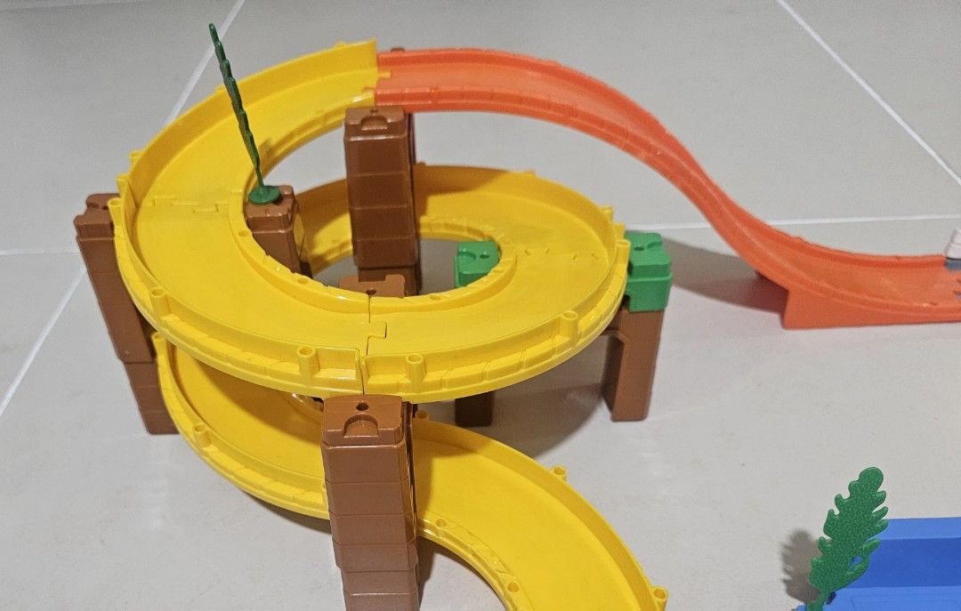 Preloved Tomica System Basic Road Set (Category: Action & Battle Toys) located in Quezon City. Submitted by newgem.b5485b (Listing ID 1465221078, Image 2). Description: Track Sections • 8x Curved Roads (Yellow) • 1x Downhill Slope Ramp (Orange) - with visible scratch • 2x Curved Roads (Gray/White) • 1x T-Junction Split Road (Gray) • 1x Parking Area Baseplate (Blue) Structural Supports (Piers / Pillars) • 4x Large Brown Pillars (Bridge piers) • 1x