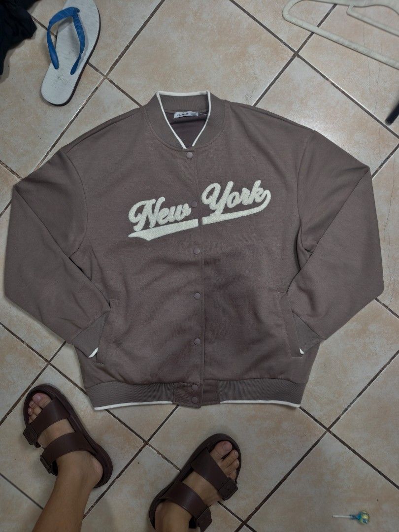 Pull&Bear New York Varsity Jacket Brown (Category: Coats, Jackets and Outerwear) located in Manila. Submitted by safetiger.42d40e (Listing ID 1465323737, Image 1). Description: - Brand: Pull&Bear - Color: Brown with cream and white details - Style: Varsity jacket with snap button closure - Design: 'New York' chenille embroidered lettering on the chest - Details: Ribbed collar, cuffs, and hem with white tipping; two front pockets - Fit & Material: