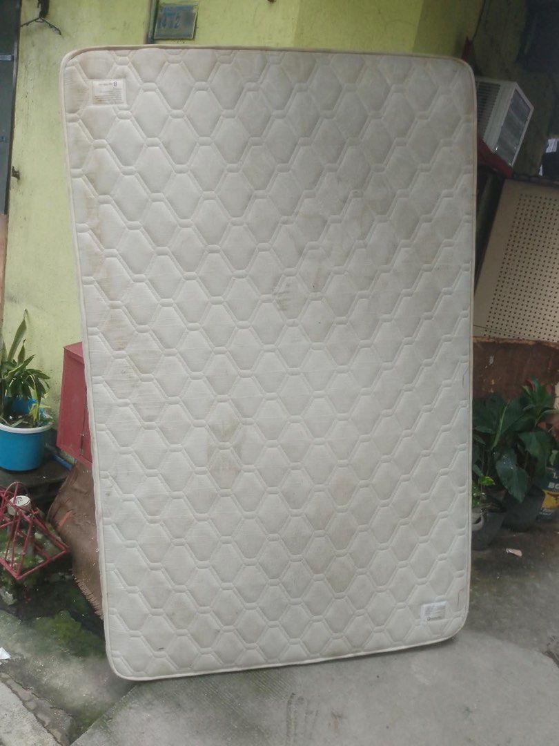 Quilted white mattress (Category: Bed Frames & Mattresses) located in Manila. Submitted by khianyanique (Listing ID 1465267689, Image 2). Description: - Type: Standard rectangular mattress - Design: Classic white quilted with diamond pattern stitching and solid edge piping - Condition: Shows visible dirt marks and staining on the fabric cover - Placement: Currently stored upright - Ideal for: Upcycling, DIY projects, or budget-friendly temporary 