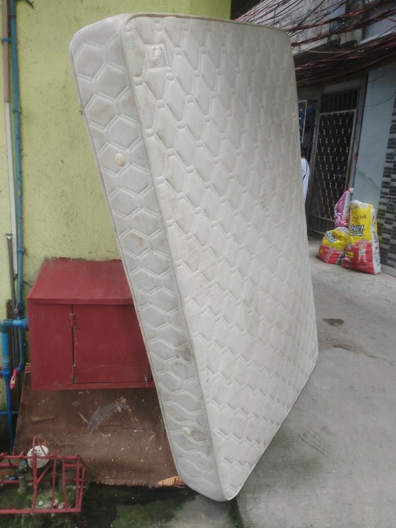 Quilted white mattress (Category: Bed Frames & Mattresses) located in Manila. Submitted by khianyanique (Listing ID 1465267689, Image 1). Description: - Type: Standard rectangular mattress - Design: Classic white quilted with diamond pattern stitching and solid edge piping - Condition: Shows visible dirt marks and staining on the fabric cover - Placement: Currently stored upright - Ideal for: Upcycling, DIY projects, or budget-friendly temporary 