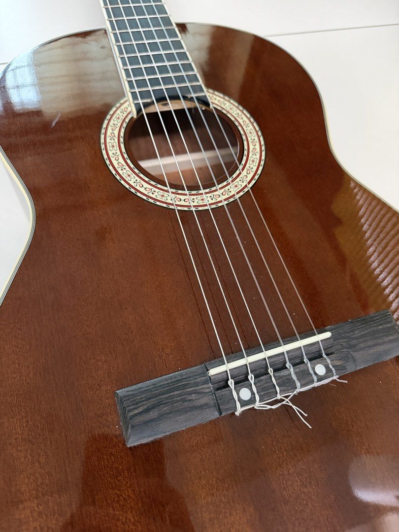 Skywing Classical Guitar (Category: Musical Instruments) located in Manila. Submitted by shopandscore (Listing ID 1465266398, Image 2). Description: - Brand: Skywing - Type: Acoustic classical guitar with standard scale length - Strings: Traditional nylon strings with tie-block bridge setup - Design: Slotted headstock with white tuning keys and gold-plated hardware - Aesthetics: High gloss finish, decorative rosette inlay around soundhole, and ri