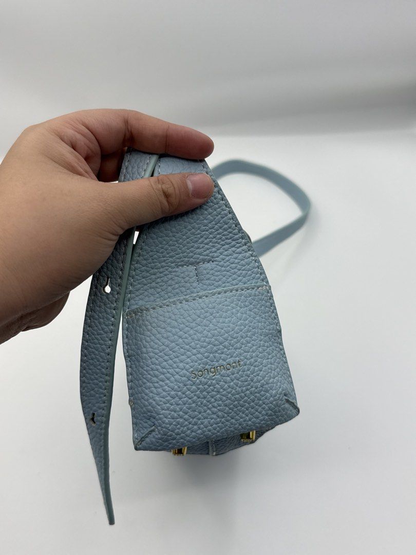 Songmont (Category: Cross-body Bags) located in Caloocan City. Submitted by rossvault2 (Listing ID 1465229781, Image 3). Description: - Brand: Songmont - Material: Premium light blue pebbled leather with chic white contrast stitching - Closure: Flap top with a modern vertical seam on the front - Strap: Long, adjustable shoulder/crossbody strap - Hardware: Elegant gold-tone feet on the bottom panel for extra protection - Details: Stamped brand log