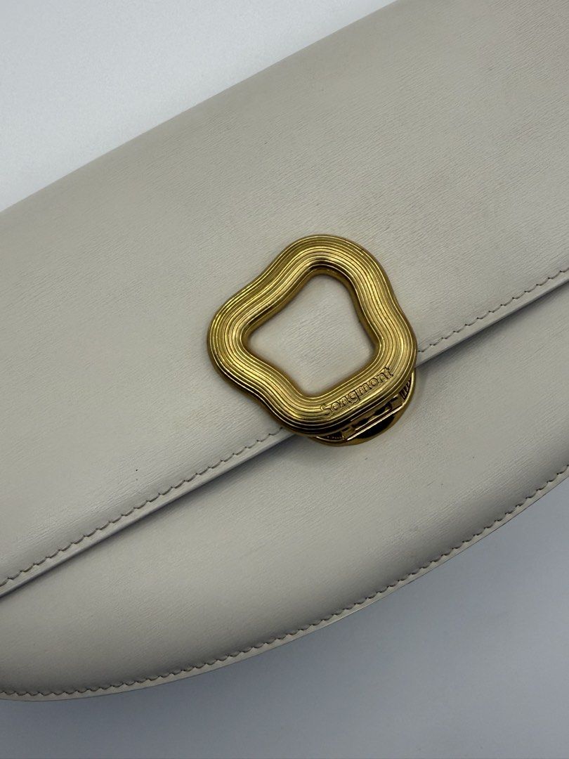 Songmont (Category: Cross-body Bags) located in Caloocan City. Submitted by rossvault2 (Listing ID 1465236822, Image 3). Description: - Brand: Authentic Songmont - Color: Off-white leather with a vibrant green interior - Hardware: Premium gold-tone hardware with a unique wavy metal front closure - Compartments: Interior zippered compartment featuring a stylish patterned fabric lining - Strap: Adjustable matching leather strap - Branding: Cleanly 
