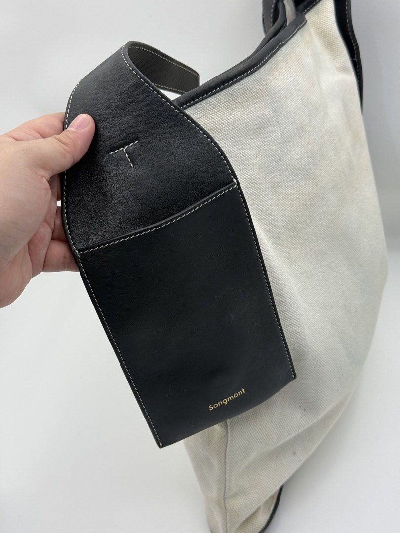 Songmont Tote Bag (Category: Tote Bags) located in Caloocan City. Submitted by rossvault2 (Listing ID 1465234996, Image 3). Description: - Brand: authentic Songmont Tote Bag - Material: Cream canvas with black leather trim, bottom panel, and matching shoulder strap - Details: Gold-foil brand stamp on the side tab and dark embossed label patch on the front - Condition: Pre-loved with noticeable light stains on the cream canvas body (priced accordi