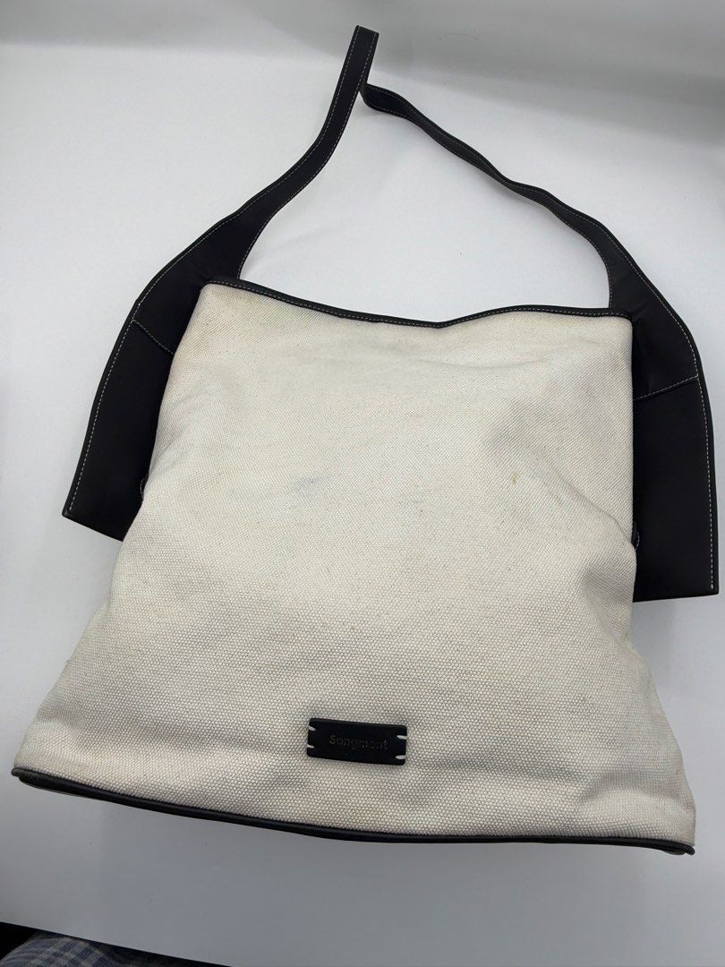 Songmont Tote Bag (Category: Tote Bags) located in Caloocan City. Submitted by rossvault2 (Listing ID 1465234996, Image 2). Description: - Brand: authentic Songmont Tote Bag - Material: Cream canvas with black leather trim, bottom panel, and matching shoulder strap - Details: Gold-foil brand stamp on the side tab and dark embossed label patch on the front - Condition: Pre-loved with noticeable light stains on the cream canvas body (priced accordi