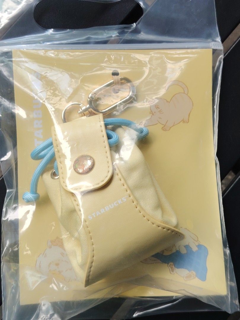Starbucks Yellow Mini Pouch Keychain Bag Cat Design (Category: Purses & Pouches) located in Quezon City. Submitted by anna.anna8 (Listing ID 1465240190, Image 1). Description: - Authentic Starbucks mini pouch - Material: Yellow canvas with chic faux leather trim - Closure: Secure blue drawstring and snap button flap - Feature: Gold-tone clasp keychain attached on top - Inclusions: Cat illustration background card - Condition: Brand new, sealed in
