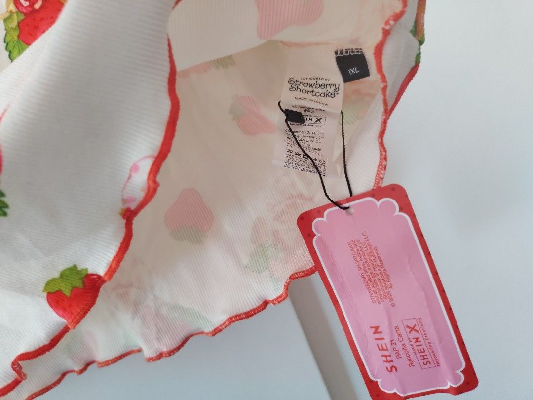 Strawberry Shortcake X SHEIN White Ribbed Top (Category: Shirts) located in Manila. Submitted by babeboxtheory (Listing ID 1465189237, Image 3). Description: - Official SHEIN x Strawberry Shortcake collaboration - Condition: Brand new with original tags attached - Size: 1XL - Design: White ribbed short-sleeve top with all-over Strawberry Shortcake print - Details: Scoop neckline with red lace trim, tiny center bow, and lettuce edge hem and sleeve