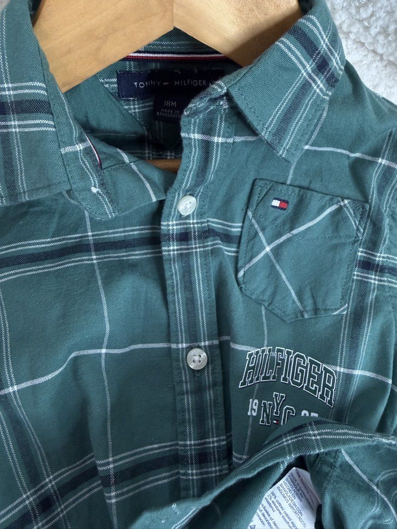 Tommy Hilfiger Green Plaid Button-Down Shirt 18M (Category: Babies & Kids Fashion) located in Manila. Submitted by happy_kidsapparel (Listing ID 1465248497, Image 2). Description: - Brand: Tommy Hilfiger - Item: Toddler Boys Button-Down Shirt - Size: 18 Months - Color/Pattern: Green plaid with navy and white lines - Material: Cotton blend (Made in Bangladesh) - Details: Chest pocket with signature flag logo, white embroidered 'HILFIGER 19 NYC 85'