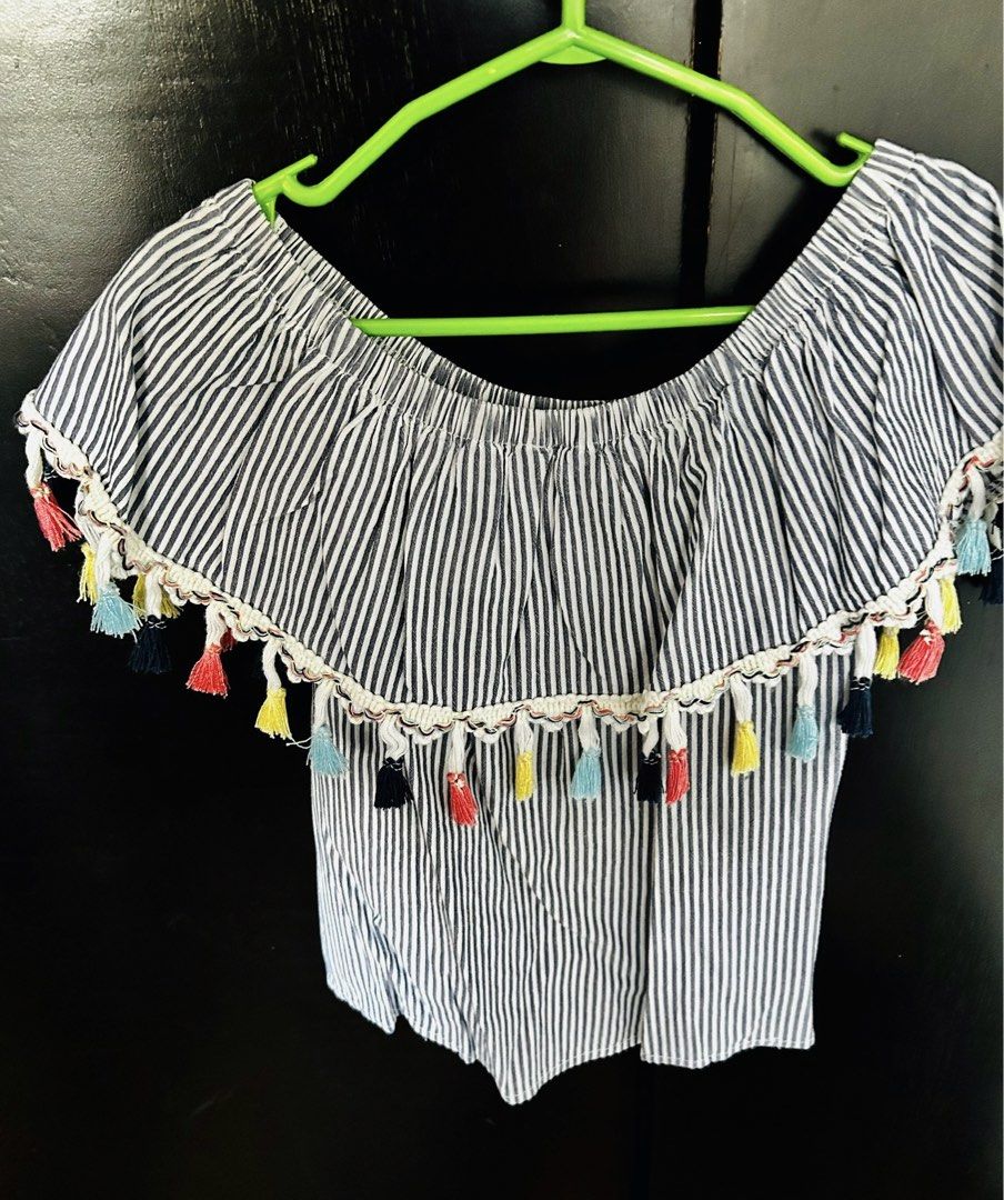 Twilo Blue & White Striped Off-Shoulder Tassel Top (Category: Babies & Kids Fashion) located in Pasig City. Submitted by royalregistry (Listing ID 1465325396, Image 2). Description: - Brand: Twilo - Size: 6 - Design: Blue and white stripes, off-shoulder with ruffle overlay and colorful tassel accents - Material: Lightweight and breathable, ideal for warm weather or beach trips.