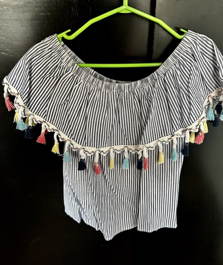 Twilo Blue & White Striped Off-Shoulder Tassel Top (Category: Babies & Kids Fashion) located in Pasig City. Submitted by royalregistry (Listing ID 1465325396, Image 1). Description: - Brand: Twilo - Size: 6 - Design: Blue and white stripes, off-shoulder with ruffle overlay and colorful tassel accents - Material: Lightweight and breathable, ideal for warm weather or beach trips.