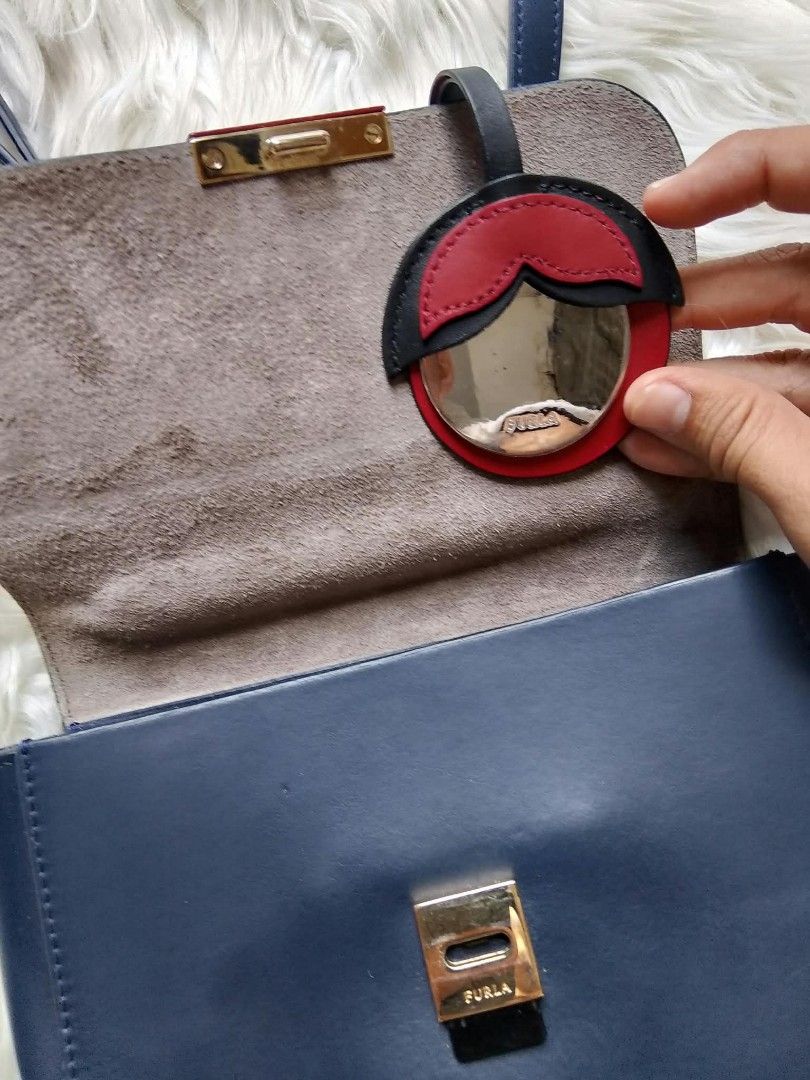 Authentic Furla 1927 Mini Top Handle with Myplay Charm™️ (Category: Luxury Bags & Wallets) located in Midsayap. Submitted by purse_gedo (Listing ID 1466997357, Image 2). Description: - Brand: Furla - Color: Navy blue leather with gold-tone hardware and red accents - Closure: Unique red rectangular clasp - Interior: Soft gray suede lining - Inclusions: Long adjustable shoulder strap and matching circular mirror charm - Condition: Clean overall, wi
