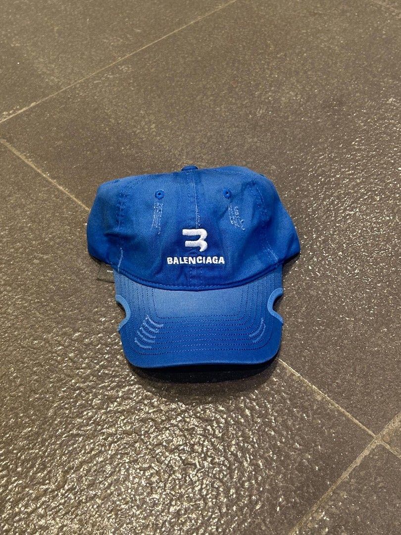 Balenciaga Blue Baseball Cap (Category: Caps & Hats) located in Pasig City. Submitted by paulclzdo (Listing ID 1467074457, Image 1). Description: - Brand: Balenciaga - Color: Bright blue with white embroidered logo - Condition: Excellent with inner tags intact - Details: Trendy distressed effects on brim and crown - Fit: Adjustable back strap with silver-tone metal buckle - Origin: Made in Italy - Perfect for daily streetwear and casual outfits.