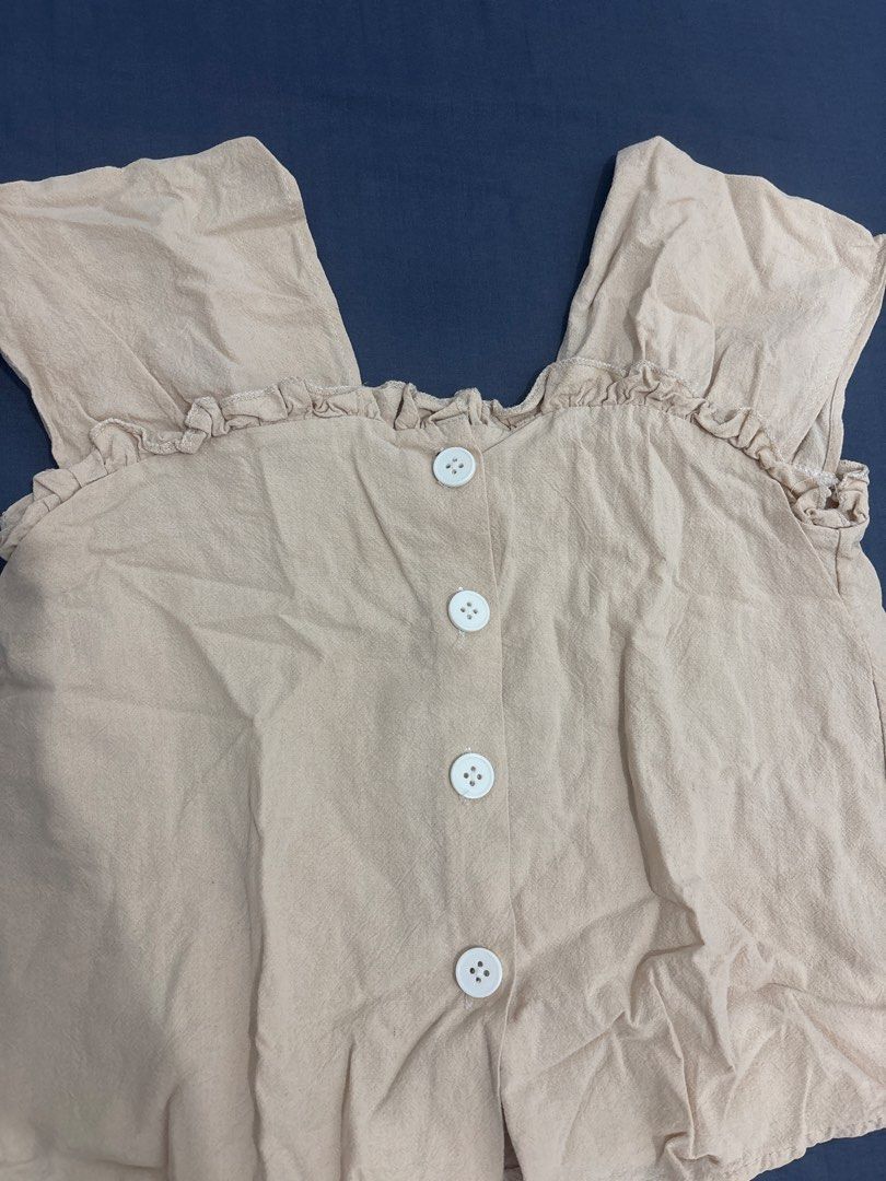 Beige Short Sleeve Ruffle Blouse with White Buttons (Category: Blouses) located in Makati City. Submitted by blueberrylime (Listing ID 1466974610, Image 2). Description: - Color: Versatile beige - Fit: Relaxed, free size - Material: Lightweight linen-like textured fabric - Design: Square neckline with cute ruffle trim on collar and shoulders - Closure: Front fastening with four round white buttons - Styling: Perfect to pair with skirts or high-wa