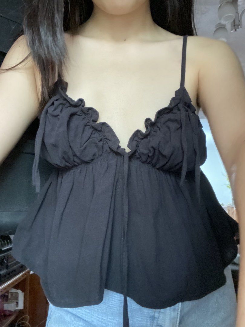 Black camisole top with ruffles and front ties (Category: Sleeveless) located in Angeles City. Submitted by kooarchives (Listing ID 1467166999, Image 2). Description: - Color: Classic black - Design: Thin straps with gathered ruffles along the V-neckline - Detail: Center tie string accent - Fit: Flowy fabric bottom layer - Styling: Perfect to pair with high-waisted denim skirts or jeans for casual days out.