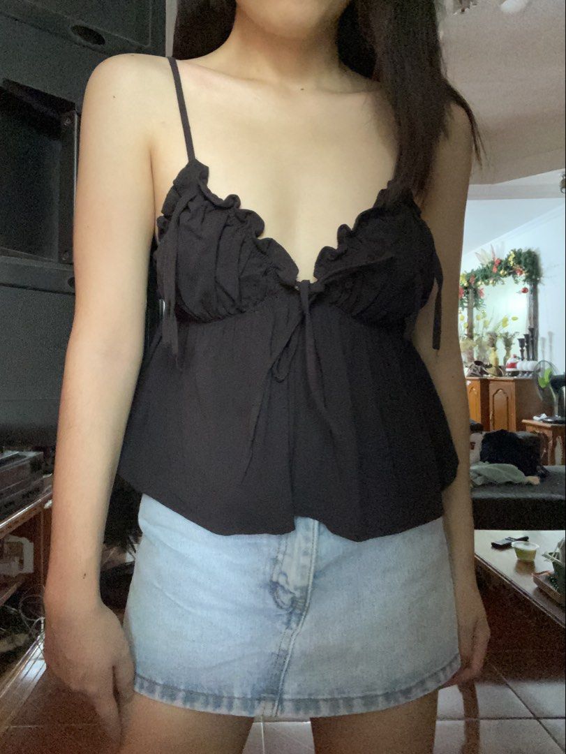 Black camisole top with ruffles and front ties (Category: Sleeveless) located in Angeles City. Submitted by kooarchives (Listing ID 1467166999, Image 1). Description: - Color: Classic black - Design: Thin straps with gathered ruffles along the V-neckline - Detail: Center tie string accent - Fit: Flowy fabric bottom layer - Styling: Perfect to pair with high-waisted denim skirts or jeans for casual days out.
