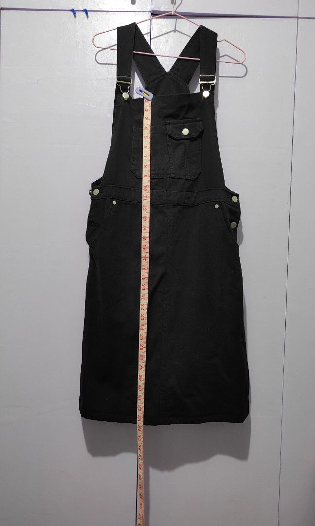Black denim jumper dress (Category: Jumpsuits) located in Bacolor. Submitted by annjjjjj (Listing ID 1467103633, Image 3). Description: - Color: Black - Material: Thick, sturdy cotton denim - Features: Adjustable shoulder straps, metal buttons, front bib pocket with buttoned flap, side pockets, and waist button closures - Cut: Straight skirt ending around the knees - Style: Minimalist basic, highly versatile for layering with tees or sweaters.