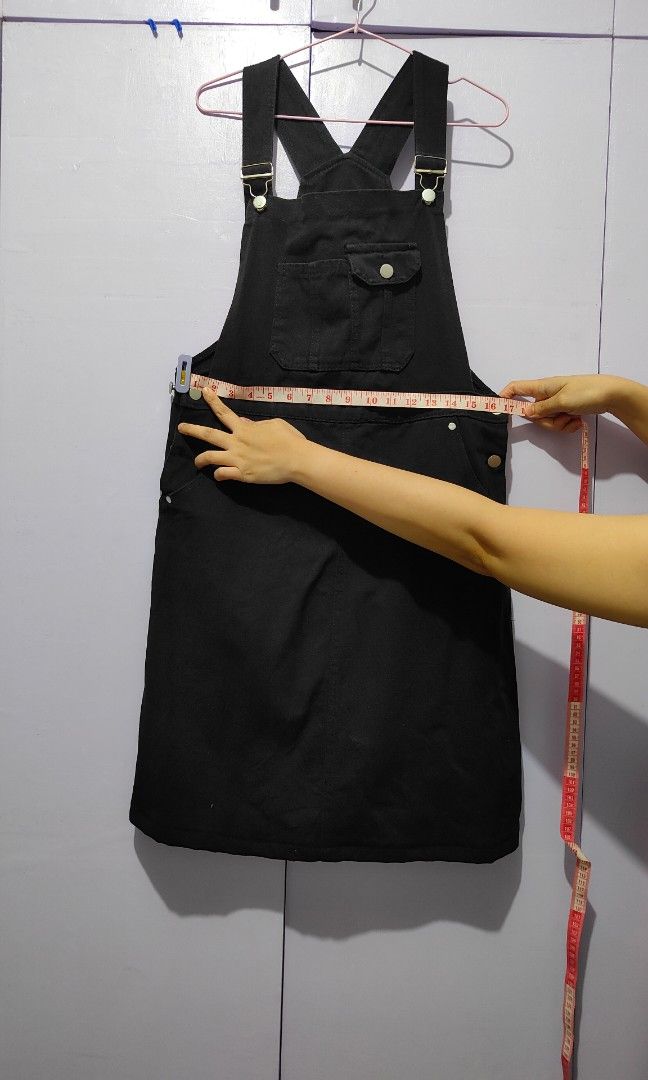 Black denim jumper dress (Category: Jumpsuits) located in Bacolor. Submitted by annjjjjj (Listing ID 1467103633, Image 2). Description: - Color: Black - Material: Thick, sturdy cotton denim - Features: Adjustable shoulder straps, metal buttons, front bib pocket with buttoned flap, side pockets, and waist button closures - Cut: Straight skirt ending around the knees - Style: Minimalist basic, highly versatile for layering with tees or sweaters.