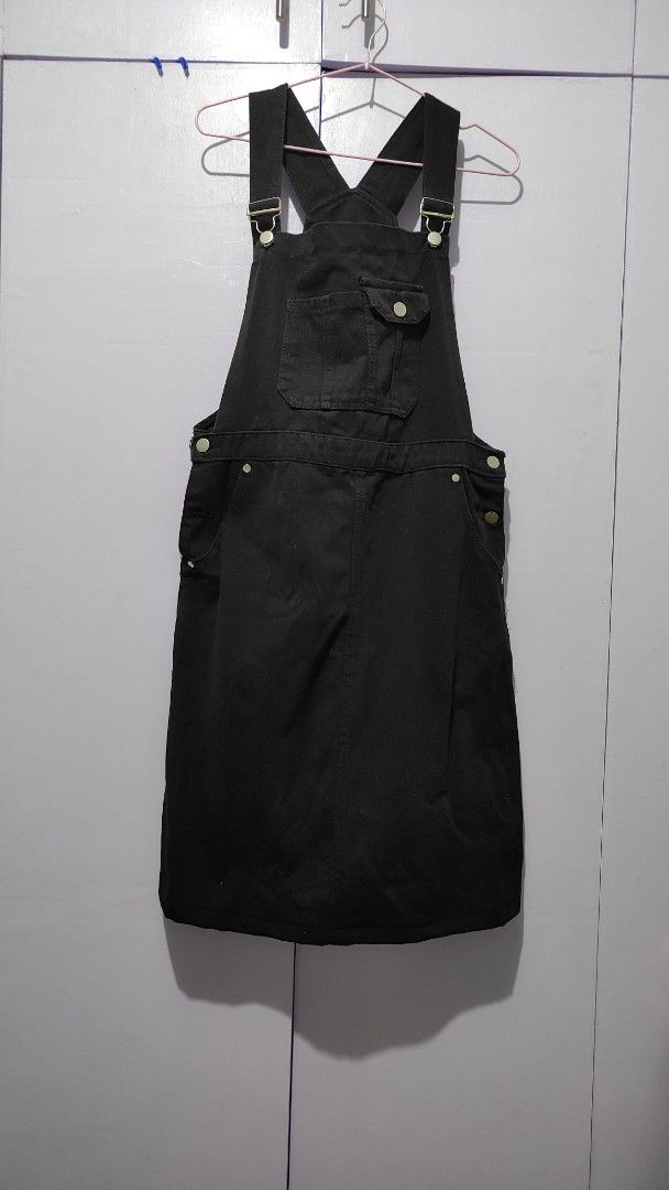 Black denim jumper dress (Category: Jumpsuits) located in Bacolor. Submitted by annjjjjj (Listing ID 1467103633, Image 1). Description: - Color: Black - Material: Thick, sturdy cotton denim - Features: Adjustable shoulder straps, metal buttons, front bib pocket with buttoned flap, side pockets, and waist button closures - Cut: Straight skirt ending around the knees - Style: Minimalist basic, highly versatile for layering with tees or sweaters.