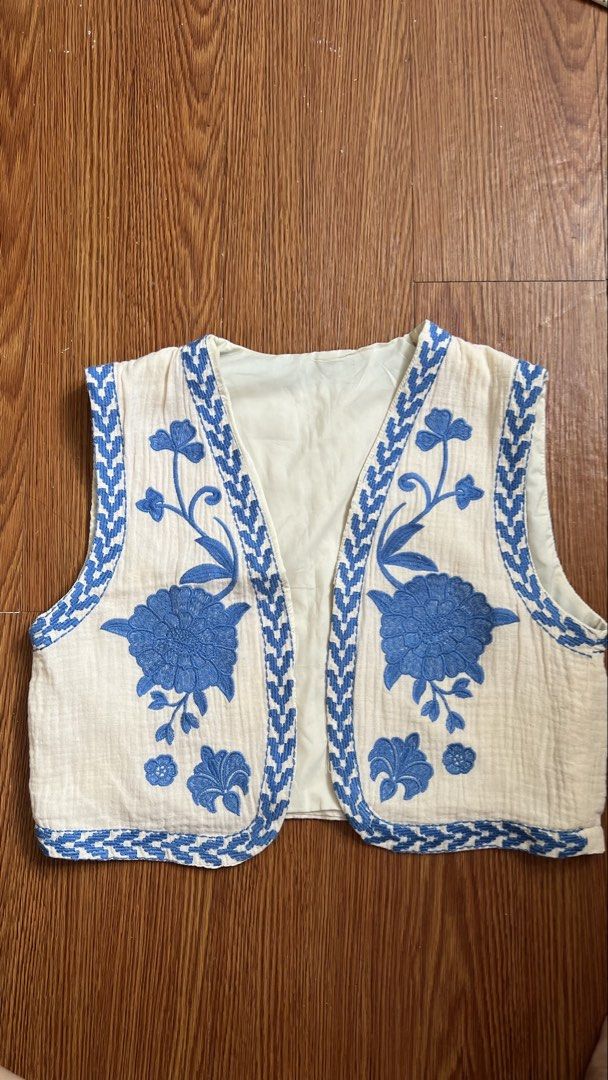 Blue Embroidered Vest (Category: Sleeveless) located in Manila. Submitted by d.rosie844 (Listing ID 1467074729, Image 1). Description: - Color: Cream with bright blue floral embroidery - Material: 100% cotton with fully lined interior - Design: Open front (no buttons), cropped length, and ethnic geometric pattern along the edges and neckline - Condition: Excellent pre-loved condition - Perfect for layering over basic tees or dresses for a bohemia