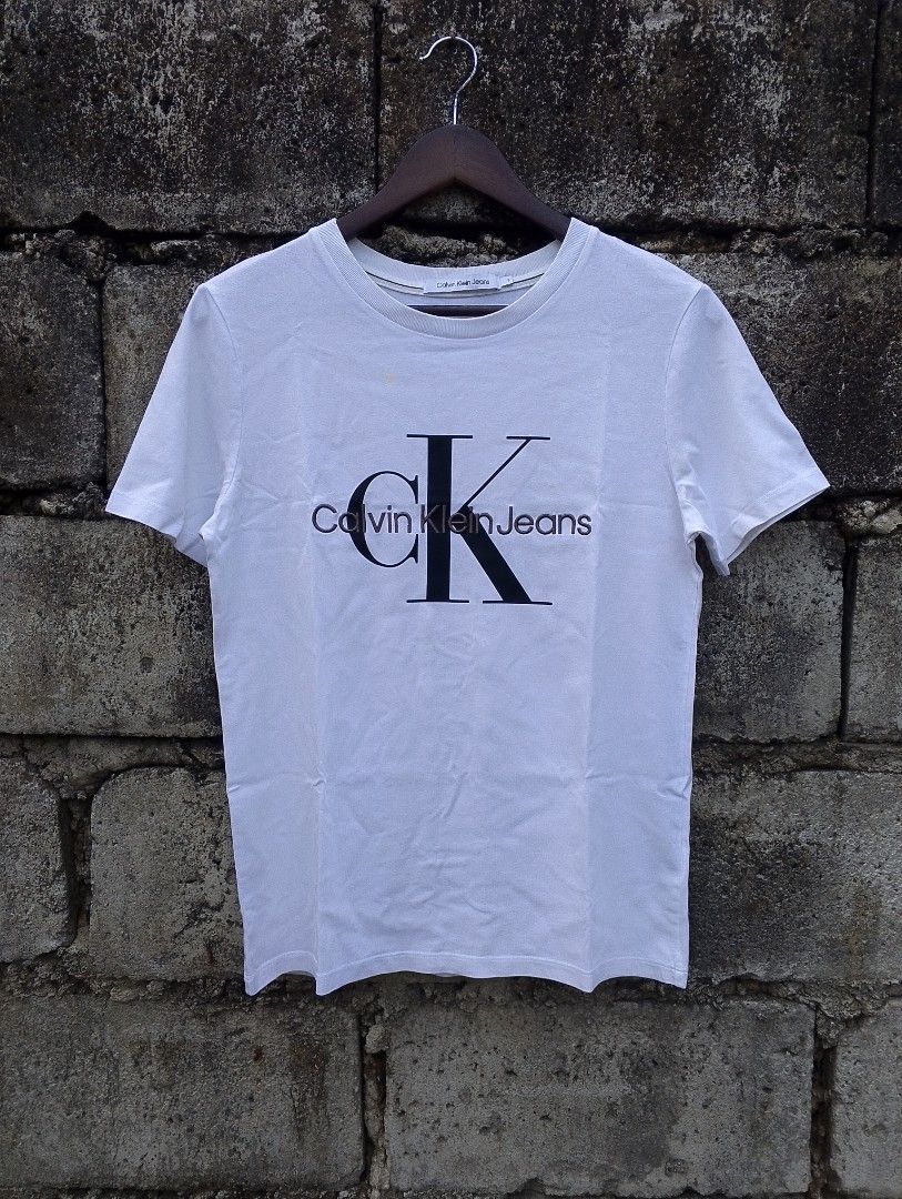 Calvin Klein Jeans Core Monogram Logo Tee (Category: Tshirts & Polo Shirts ) located in Baliuag. Submitted by retrovault83 (Listing ID 1467131142, Image 2). Description: ✨ Condition: 9/10 – Excellent Preloved Condition 📏 Measurements (Flat Lay, Tagged Size S): • Pit to Pit: 18 • Length: 25 ✅ Details: • Calvin Klein Jeans Graphic T-Shirt • Clean white body featuring classic black "cK" big logo print with embroidered "Calvin Klein Jeans" front tex
