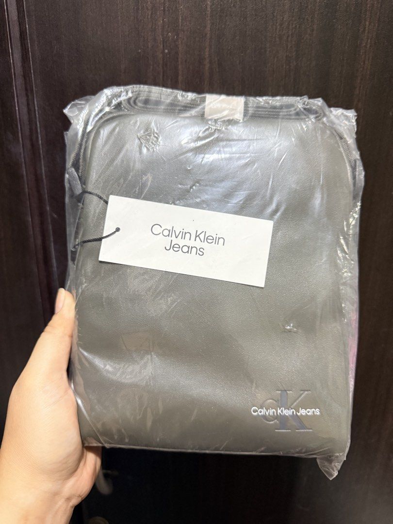 Calvin Klein Jeans Crossbody Bag (Category: Sling Bags) located in Quezon City. Submitted by gel.cortez (Listing ID 1467009892, Image 2). Description: - Brand: Calvin Klein Jeans - Style: Crossbody bag - Color: Olive grey - Material: Faux leather with printed logo near the bottom corner - Strap: Adjustable and neatly folded on top - Condition: Brand new, clean with no defects, sealed in original plastic packaging with tags attached - Availble als