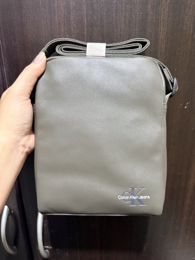 Calvin Klein Jeans Crossbody Bag (Category: Sling Bags) located in Quezon City. Submitted by gel.cortez (Listing ID 1467009892, Image 1). Description: - Brand: Calvin Klein Jeans - Style: Crossbody bag - Color: Olive grey - Material: Faux leather with printed logo near the bottom corner - Strap: Adjustable and neatly folded on top - Condition: Brand new, clean with no defects, sealed in original plastic packaging with tags attached - Availble als