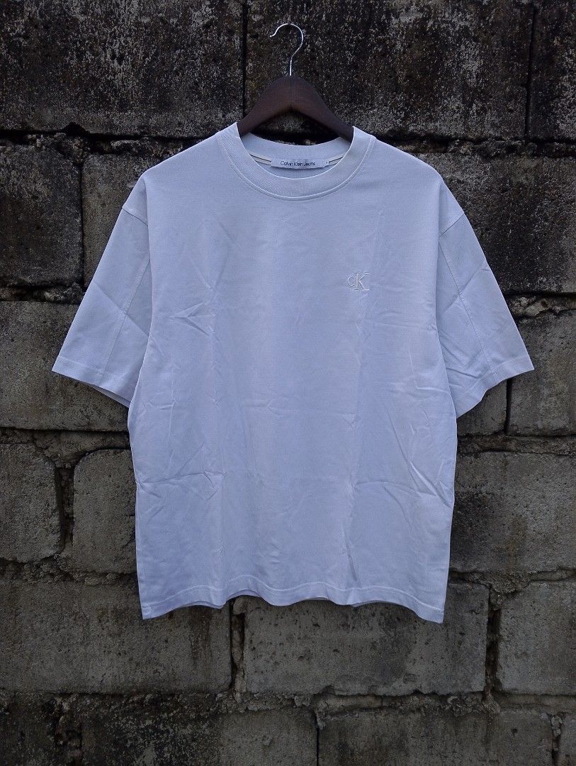 Calvin Klein Jeans Embroidered Monogram Graphic Tee (Category: Tshirts & Polo Shirts ) located in Baliuag. Submitted by retrovault83 (Listing ID 1467132047, Image 3). Description: ✨ Condition: 9/10 – Excellent Preloved Condition 📏 Measurements (Flat Lay, Tagged Size S - Relaxed Fit): • Pit to Pit: 23 • Length: 27.5 ✅ Details: • Clean white body featuring a minimal embroidered tonal "cK" logo on the left chest • Eye-catching abstract back graphic