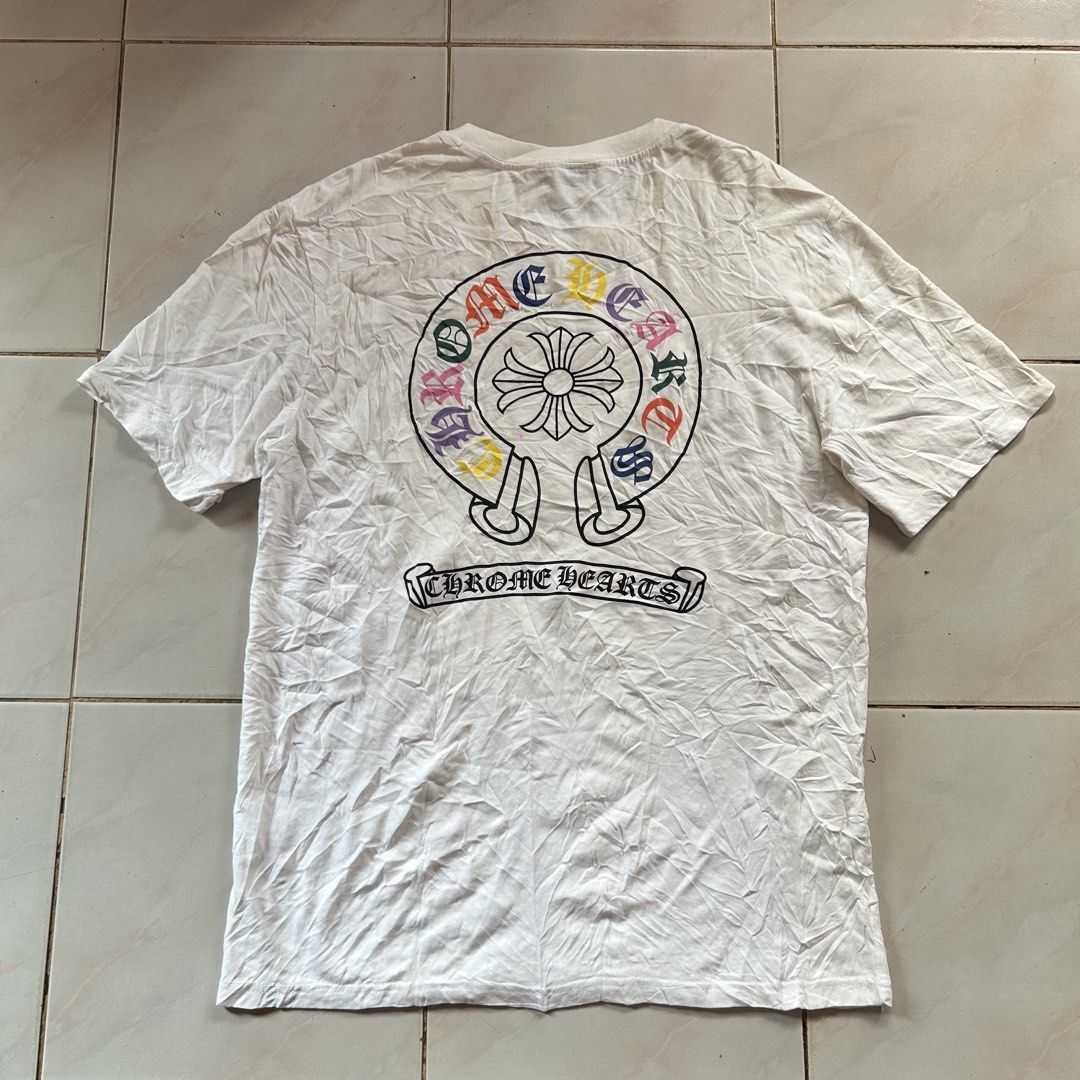 Chrome Hearts Multi Color Shirt 🔥 (Category: Tshirts & Polo Shirts ) located in Jinoba-an. Submitted by eegiboy (Listing ID 1467025464, Image 1). Description: - Brand: Chrome Hearts - Style: Short sleeve tee with standard fit - Color: White - Details: Black leather cross patch on chest, large multi-color horseshoe graphic and gothic text banner on the back - Material: 100% Cotton - Condition: Pre-loved with minor yellowing around the neckline fr