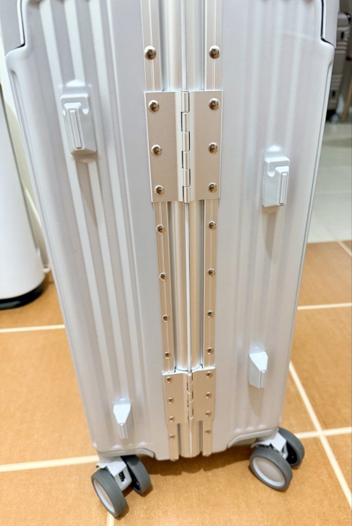 Compass Luggage Silver Hard Case Suitcase TSA Lock (Category: Luggage) located in Mandaluyong City. Submitted by miss_a18 (Listing ID 1467105296, Image 3). Description: Silver Compass hardshell luggage with vertical ribbed texture. Integrated TSA-approved combination lock on top. Sturdy aluminum frame closure with multiple metal hinges down the side. Dual wheels on all four corners for smooth rolling. Grey fabric interior lining includes zippered