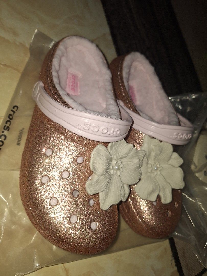 Crocs Classic Lined Glitter Clog Barely Pink (Category: Slippers and slides) located in Cavite. Submitted by lilltevg (Listing ID 1467139316, Image 2). Description: Rose gold glitter finish all over. Soft fuzzy pink lining inside. Large white flower charm attached on top. Light pink strap with Crocs branding. Slip-on style, super comfy. Size J4/w6. Brand new with tags and original packaging..
