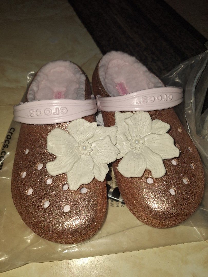 Crocs Classic Lined Glitter Clog Barely Pink (Category: Slippers and slides) located in Cavite. Submitted by lilltevg (Listing ID 1467139316, Image 1). Description: Rose gold glitter finish all over. Soft fuzzy pink lining inside. Large white flower charm attached on top. Light pink strap with Crocs branding. Slip-on style, super comfy. Size J4/w6. Brand new with tags and original packaging..