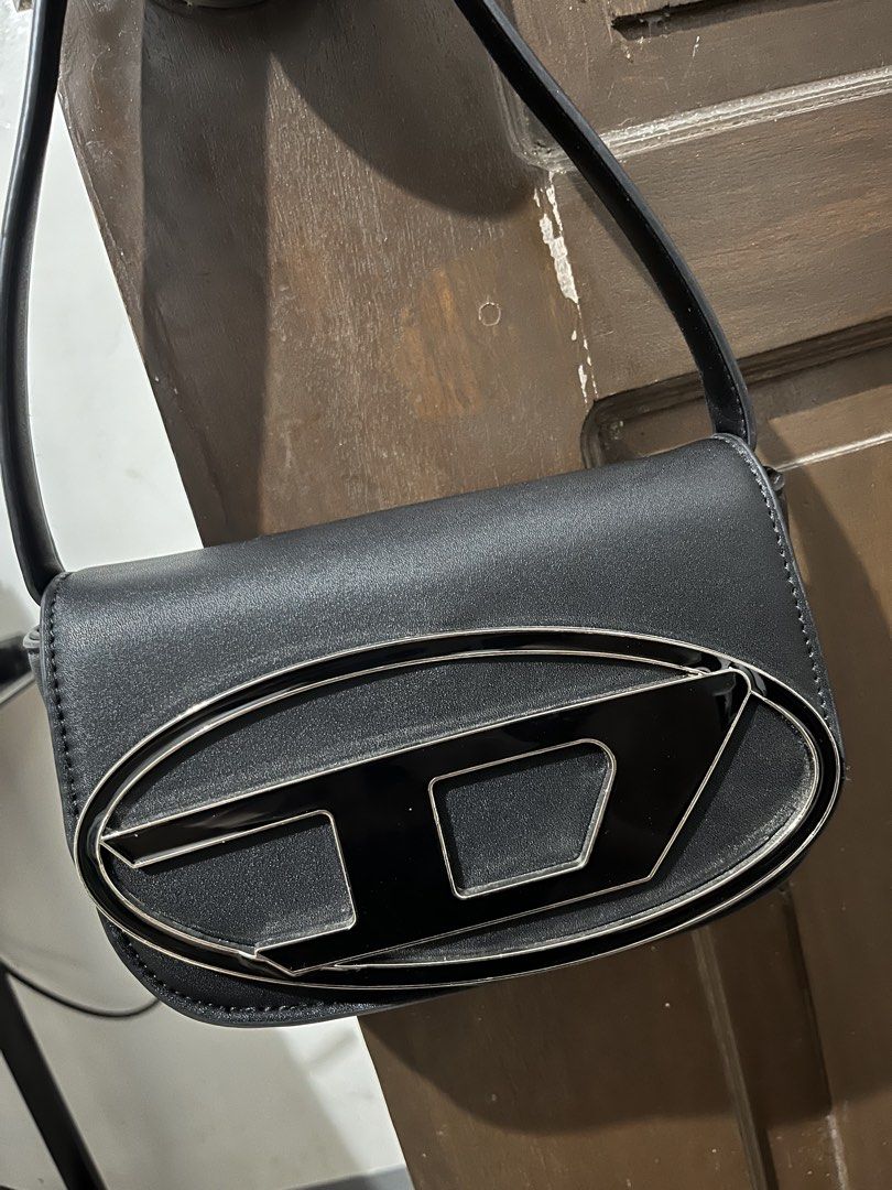 Diesel Black Oval D Logo Shoulder Bag (Category: Shoulder Bags) located in Mabalacat. Submitted by onlygrail.pamp (Listing ID 1467143969, Image 1). Description: Black leather shoulder bag from Diesel. Silver hardware with prominent metal Oval D logo on the front flap. Magnetic snap closure. Interior lined with black fabric and features a leather brand patch plus slip pocket. Clean structure with sturdy strap attached by metal rings..