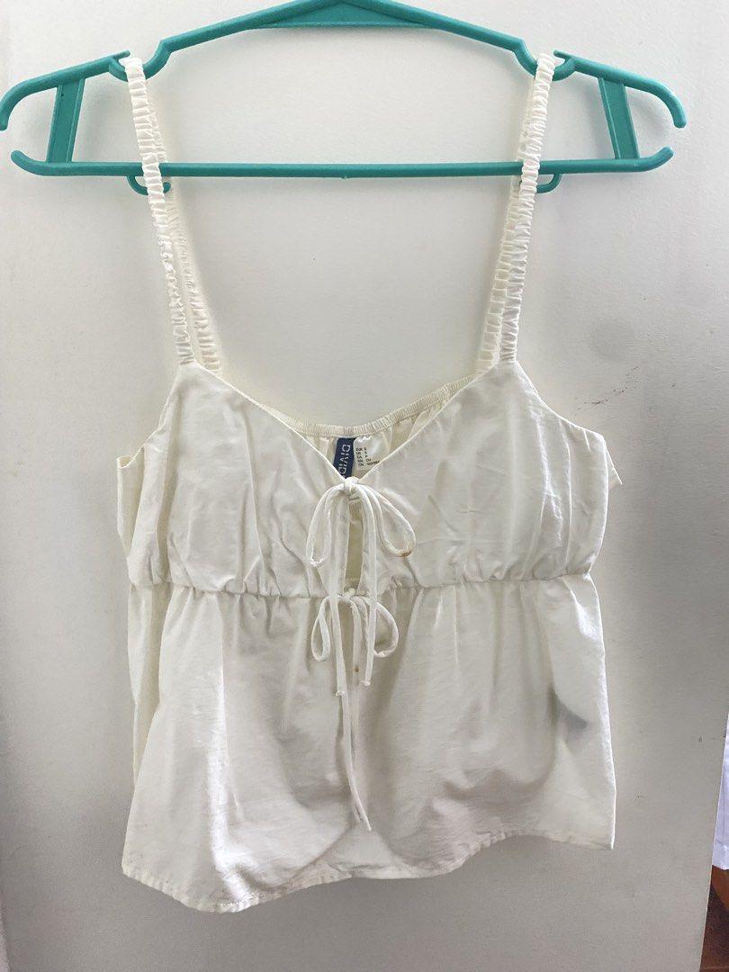Divided H&M White Tie-Front Camisole Top (Category: Sleeveless) located in Angeles City. Submitted by kooarchives (Listing ID 1467068077, Image 2). Description: - Brand/Model: Divided by H&M - Size: S (Small) - Color: White - Details: Double tie-front closures, adjustable gathered straps, peplum hem - Material: Lightweight and breathable - Condition: Clean overall, with a small brownish stain on one ribbon tie (please check photos), can be remove