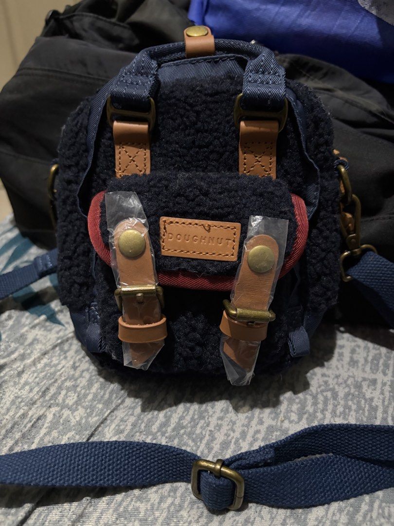 Doughnut Navy Blue Mini Crossbody Bag (Category: Cross-body Bags) located in Manila. Submitted by jjprelovedcollections2 (Listing ID 1467063285, Image 1). Description: - Brand: Doughnut - Color: Navy blue fluffy fleece with brown leather accents - Features: Front buckle pocket, inner slip pocket, and metal hardware - Condition: Brand new, hardware still wrapped in plastic with official authenticity QR hangtag attached - Strap: Detachable blue sho