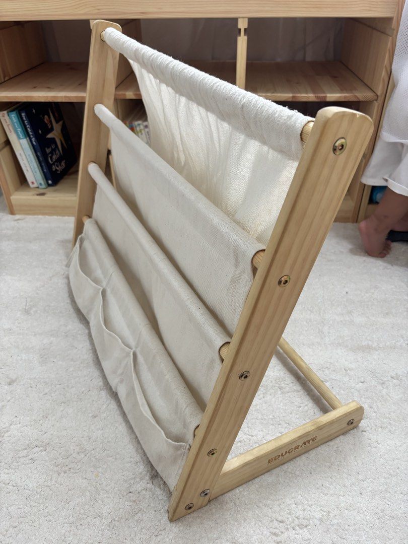 Educrate Multi Layer Montessori Sling Bookshelf (Category: Other Kids Furniture) located in Manila. Submitted by sugarcervantes (Listing ID 1466997249, Image 3). Description: - Brand: Educrate - Material: Natural wood frame with cream canvas fabric pockets - Storage: 4 spacious tiers for picture books + 3 extra small front pockets for toys and small items - Design: Sturdy, floor-standing A-frame - Perfect for: Organizing a child's reading nook or