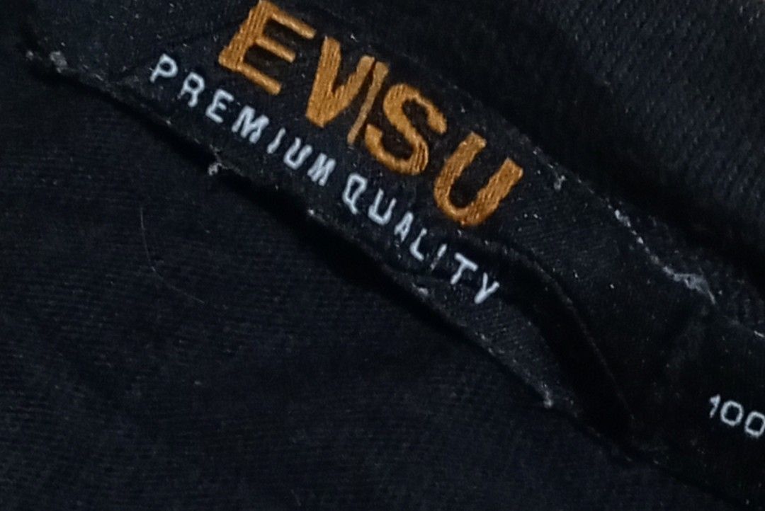 Evisu Black Graphic T-Shirt (Category: Tshirts & Polo Shirts ) located in Manila. Submitted by kents_thrift (Listing ID 1466971374, Image 3). Description: - Brand: Evisu Premium Quality - Color: Black - Size: 100 - Design: Small white seagull logo on left chest, large graffiti-style lettering across upper back, and round crest graphics on both sleeves - Authenticity: Includes official interior authentication label and collar tag.