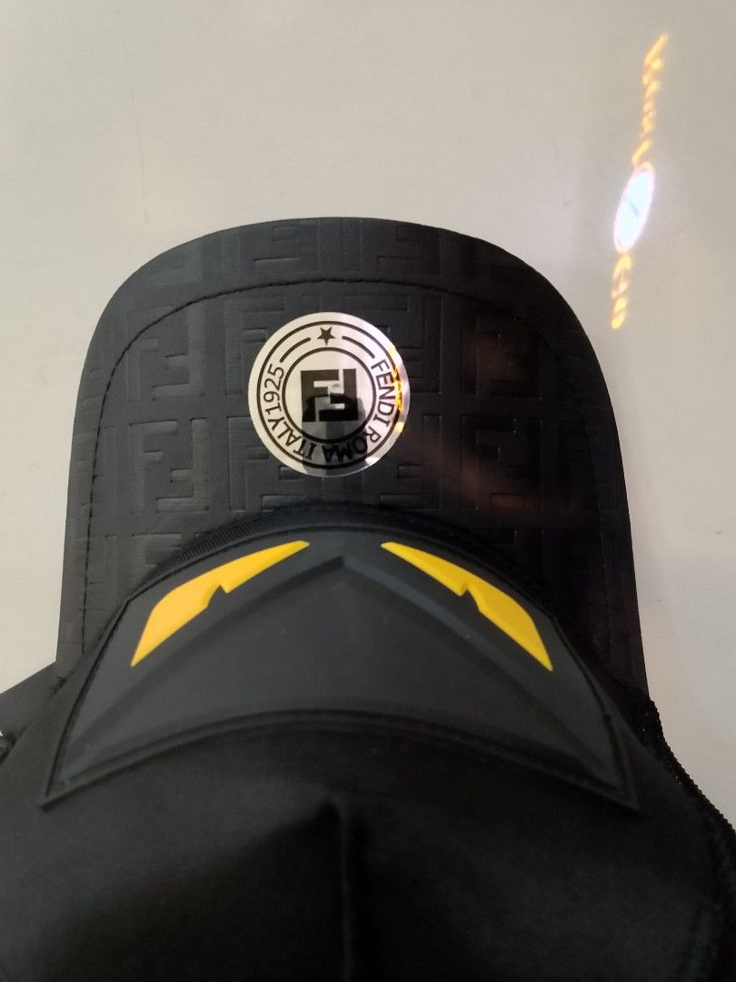 Fen di Monogram Eyes Black Trucker Cap (Category: Caps & Hats) located in Quezon City. Submitted by viaggo.travels (Listing ID 1467037462, Image 3). Description: - Brand: Fen. di - Color: Classic Black with Yellow Eye rubberized patch - Style: Trucker cap with breathable mesh back panels - Details: Embossed FF monogram pattern on the brim with original sticker - Hardware: Adjustable back strap featuring a small Fendi logo plate - Interior: Brande