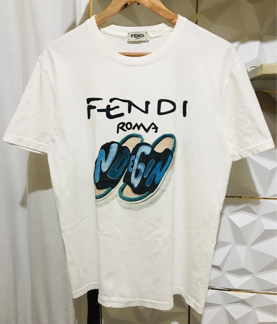 Fendi Roma Graphic Print White T-Shirt (Category: Luxury Apparel) located in Rizal. Submitted by drthriftone (Listing ID 1466972779, Image 1). Description: White graphic tee from Fendi Roma. Front features distinctive artwork with sandals and bold blue lettering. Crew neck design and short sleeves. Tag marked 21x27. Standard cotton t-shirt cut. Clean surface, solid collar ribbing, brand tag stitched at the inner neckline. Ready to wear..