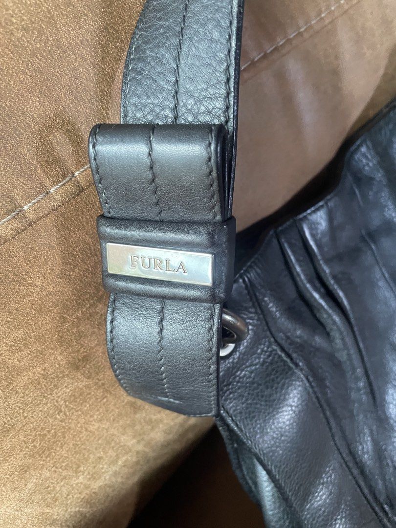 Furla Black Leather Shoulder Bag (Category: Luxury Bags & Wallets) located in Muntinlupa City. Submitted by phbudgetluxuryfinds (Listing ID 1466986959, Image 2). Description: - Brand: Furla - Material: Genuine black leather - Design: Elegant ruched front panel with silver-tone hardware - Strap: Single strap featuring an embossed metal logo plaque on the base - Interior: Cute black fabric lining with white polka dots and a convenient zippered side