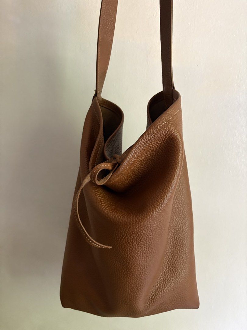 Genuine Leather Bucket Tote Bag (Category: Shoulder Bags) located in Pasig City. Submitted by makeuplover219 (Listing ID 1467010156, Image 1). Description: - Material: Genuine brown pebble leather with a slouchy, relaxed shape - Closure: Convenient drawstring closure on the side - Interior: Spacious main compartment with a trendy grey and white chevron lining - Pockets: Secure interior zipper pocket and branded leather logo patch - Comfort: Comfo