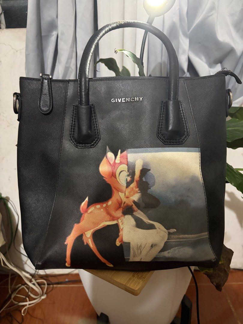 Givenchy Bambi Black Tote Bag (Category: Tote Bags) located in Manila. Submitted by lynnalec25 (Listing ID 1467148202, Image 1). Description: Givenchy black tote bag with dual top handles. Distinct Bambi graphic print printed prominently on the front. Saffiano leather texture throughout the dark body. Silver lettering stamped on the upper front. Structured upright silhouette with top zipper closures. Metal hardware rings on the side panels for at