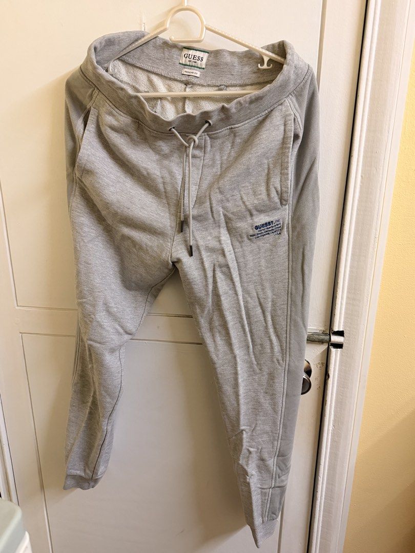 Guess Grey Regular Fit Sweatpants (Category: Joggers) located in Manila. Submitted by lanzblade (Listing ID 1467063600, Image 1). Description: - Brand/Style: Guess regular-fit grey sweatpants - Waist: Drawstring waist with metal aglets - Details: Small blue embroidered logo and address text on the front left leg - Pockets: Convenient side pockets and a single welt pocket on the back right - Cuffs: Ribbed cuffs at the ankles - Material: Soft cotto