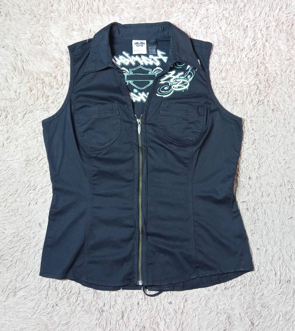 Harley Davidson Black Embroidered Zip Vest Size L (Category: Vests) located in Lucban. Submitted by aeronroyyy (Listing ID 1466988362, Image 1). Description: Black Harley-Davidson sleeveless zip-up vest in size Large. White and green embroidery lettering and graphics across the back and front chest. Metal branded zipper pull. Corset-style lace-up back detail with grommets. Collared neckline with two front chest pockets. 98 percent cotton and 2 pe