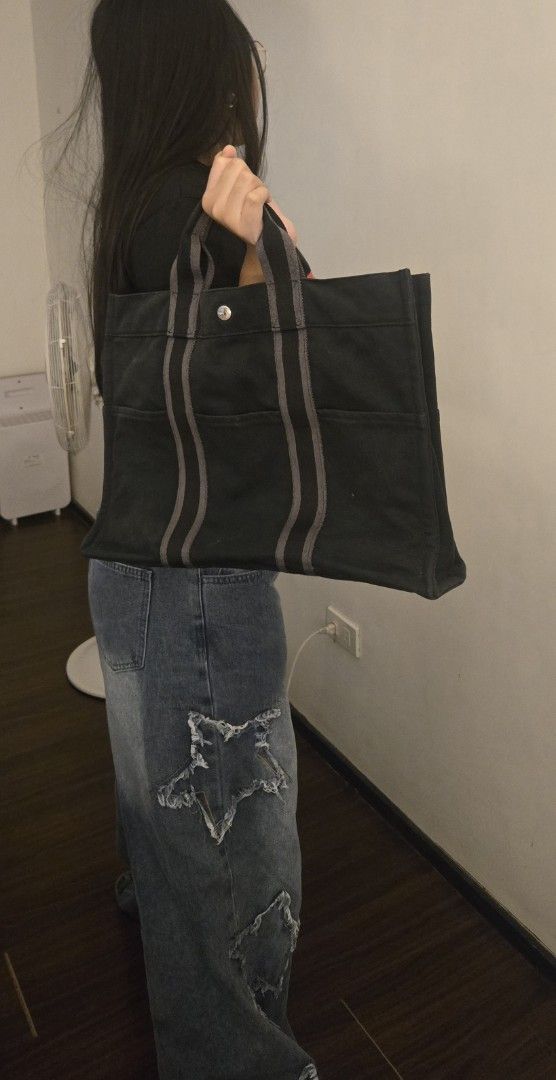 Authentic Hermes Fourre Tout Tote Bag Black Canvas (Category: Tote Bags) located in Quezon City. Submitted by PreLovedByMrsAL (Listing ID 1467038989, Image 3). Description: - Brand: Hermès Fourre Tout Tote - Material: Durable solid black canvas with dark grey straps and top handles - Closure: Silver-tone snap button at the top center - Pockets: Multiple exterior slip pockets on front and back for easy storage - Design: Structured rectangular shap