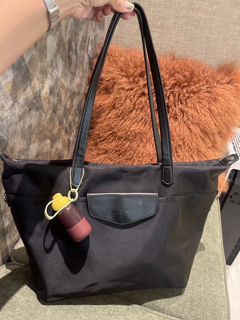 Hexagona Paris Black Nylon Tote (Category: Tote Bags) located in Pasig City. Submitted by jnzmrq1003 (Listing ID 1467047884, Image 1). Description: - Brand: Hexagona Paris - Material: Durable black nylon with black leather double shoulder straps - Storage: Top zip closure, front flap pocket with embossed branding, and back zipper access - Extras: Includes a stylish yellow and maroon capsule-shaped charm - Condition: spilled superglue inside one o