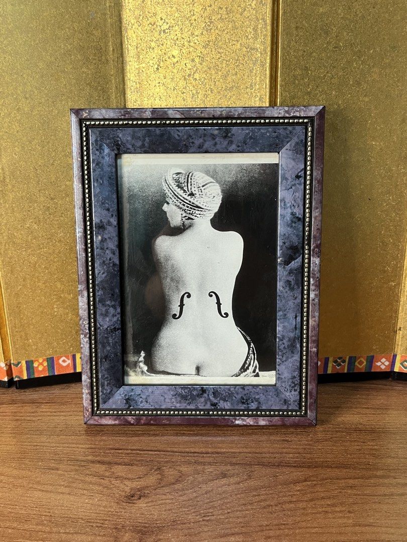 Man Ray Le Violon d'Ingres Framed Print Art (Category: Frames & Pictures) located in Gapan. Submitted by lunashop14 (Listing ID 1467095602, Image 1). Description: - Art Piece: Framed photographic print of Man Ray's famous 'Le Violon d'Ingres' - Design: Iconic black and white image of a woman's back with violin f-holes - Frame: Eye-catching purple marbled pattern with a beaded inner trim - Build: Sturdy wooden backing board secured with swivel cli