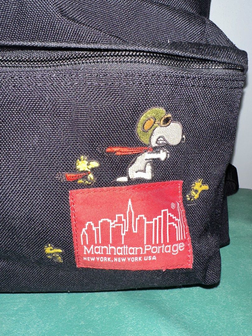 Manhattan Portage x Peanuts Snoopy Backpack (Category: Backpacks) located in Quezon City. Submitted by swift.thriftz (Listing ID 1467127659, Image 2). Description: - Limited edition Manhattan Portage x Peanuts collaboration backpack - Durable black canvas material with classic red logo patch - Features embroidered Flying Ace Snoopy and Woodstock on the front pocket - Unique camouflage inner lining with 65th anniversary Peanuts tag - Secure zipper