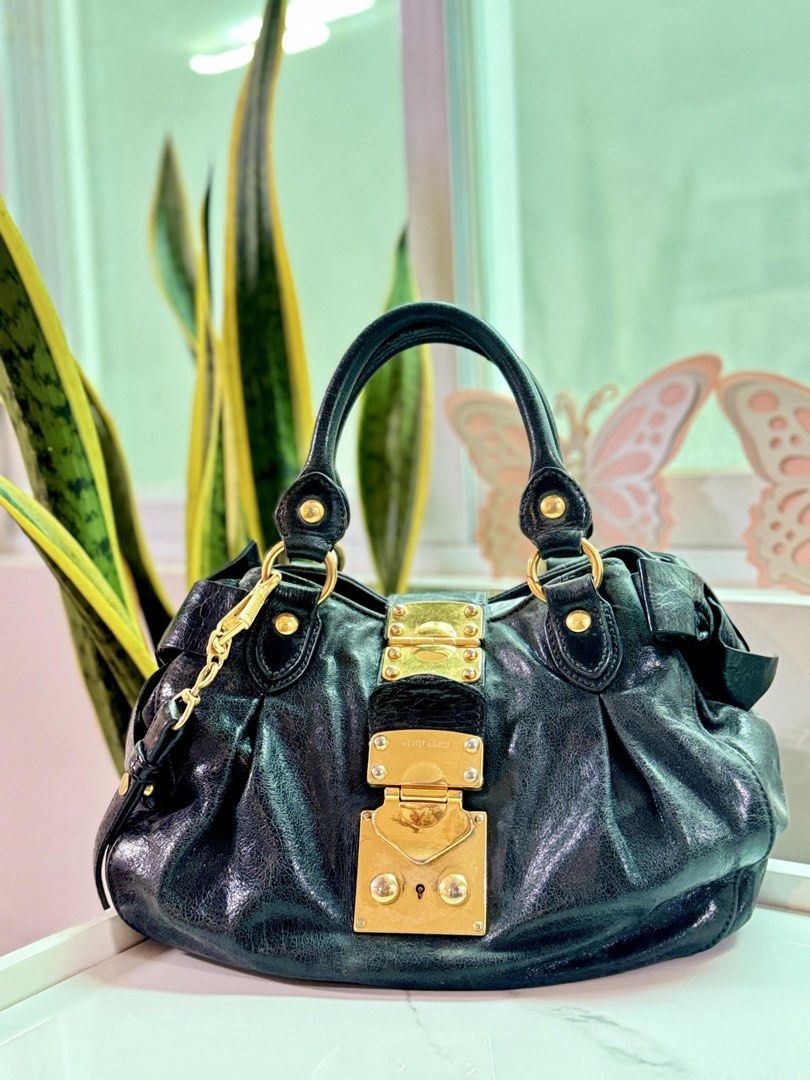 Miu Miu Black Leather Bag (Category: Luxury Bags & Wallets) located in Cainta. Submitted by thekikaymachine (Listing ID 1465131636, Image 1). Description: - Brand: Miu Miu - Material: Black crinkled leather with gold hardware - Closure & Logo: Big front metal lock and gold lettering logo on the back - Straps: Dual top handles and a detachable long leather strap - Details: Gathered sides with cute bow accents and a roomy interior - Condition: Show