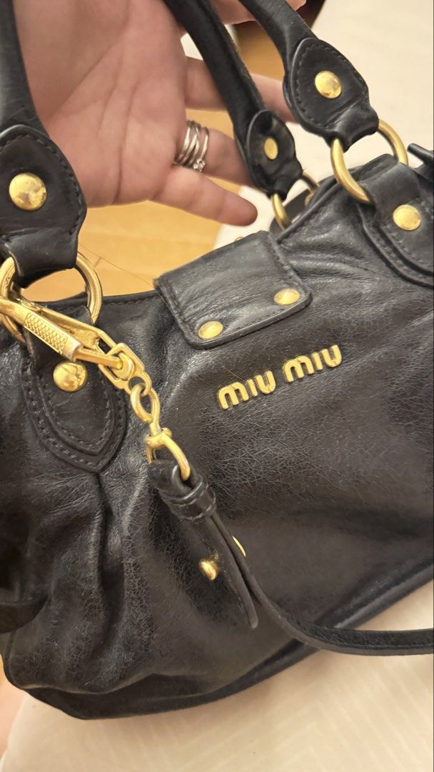 Miu Miu Black Leather Bag (Category: Luxury Bags & Wallets) located in Cainta. Submitted by thekikaymachine (Listing ID 1465131636, Image 2). Description: - Brand: Miu Miu - Material: Black crinkled leather with gold hardware - Closure & Logo: Big front metal lock and gold lettering logo on the back - Straps: Dual top handles and a detachable long leather strap - Details: Gathered sides with cute bow accents and a roomy interior - Condition: Show