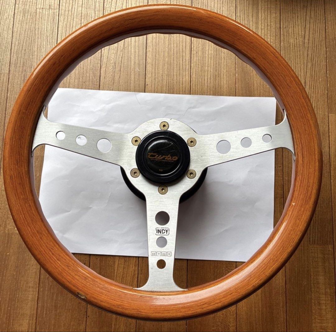 Momo Indy Wood Steering Wheel (Category: Steering, Brakes, Control Parts and Accessories) located in Muntinlupa City. Submitted by vintageboxfinds (Listing ID 1467044174, Image 1). Description: - Authentic Momo Indy wood steering wheel - Features stylish silver slotted spokes and included horn button - Classic vintage style with a natural wood grain rim finish - Ideal upgrade for older car setups and interior restoration projects - Condition: Bra